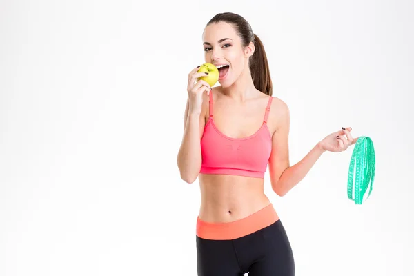 Mulher fitness positivo segurando fita métrica e comer uma maçã — Fotografia de Stock
