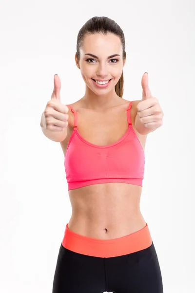 Sonriendo alegre chica de fitness mostrando los pulgares hacia arriba con ambas manos —  Fotos de Stock