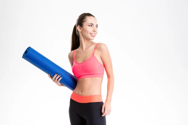 Alegre bela mulher fitness segurando tapete de ioga e olhando para longe — Fotografia de Stock