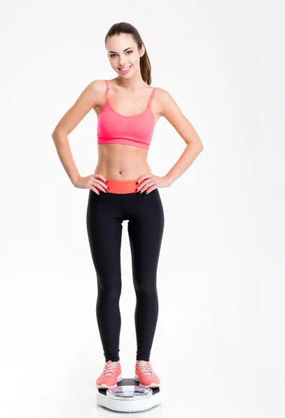 Attactive smiling young fitness woman standing on weighing scale — ストック写真