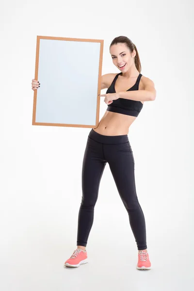 Sportswoman holding blank board and pointing on it — Stock fotografie