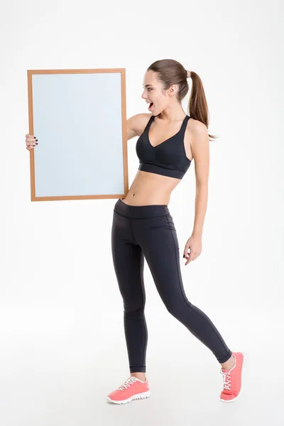 Mulher fitness jovem feliz bonita em traje mostrando placa em branco — Fotografia de Stock