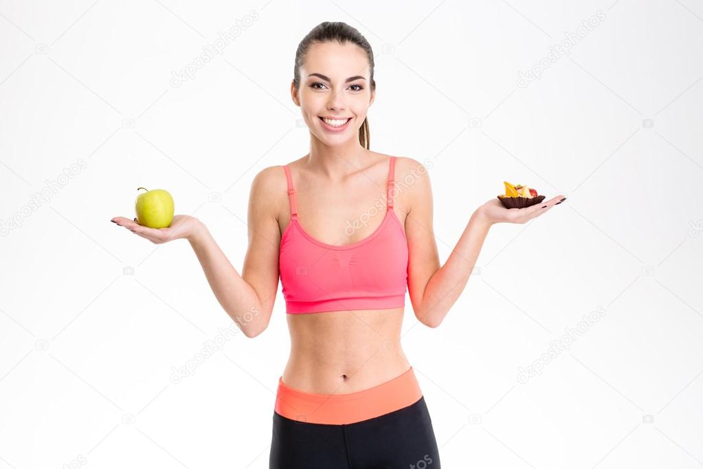 Cheerful young fitness girl holding healthy and unhealthy food