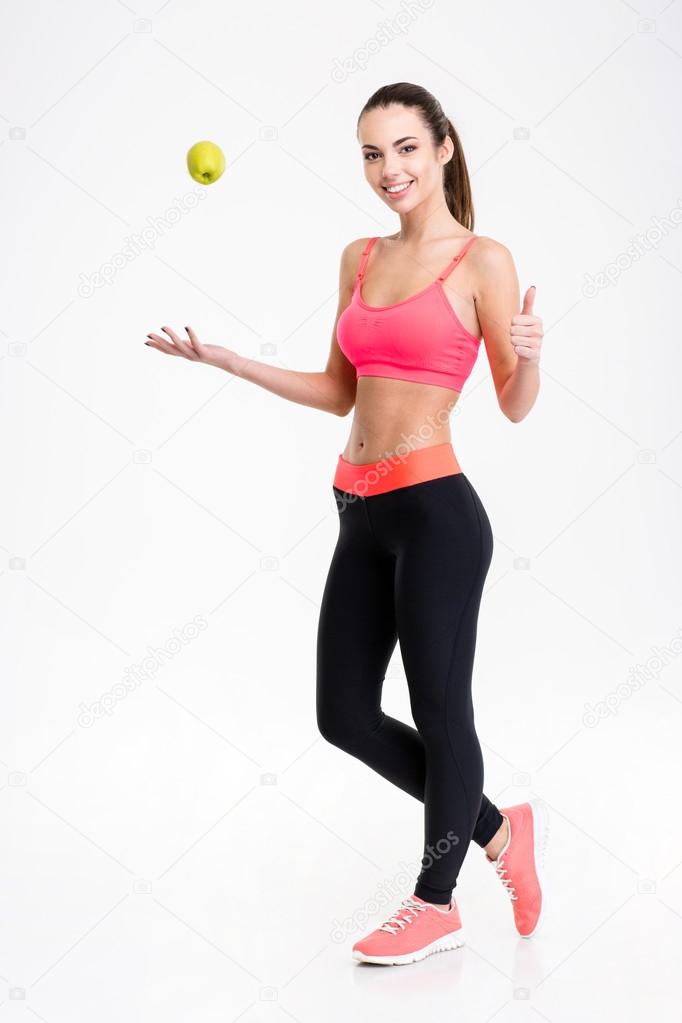 Cheerful fitness woman throwing an apple and showing thumbs up