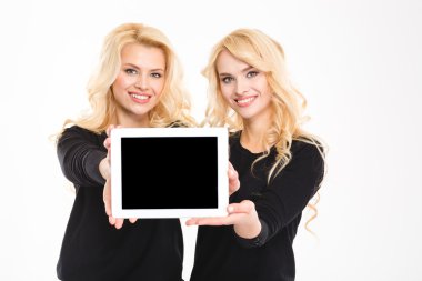Two cute lovely sisters twins showing blank tablet computer screen