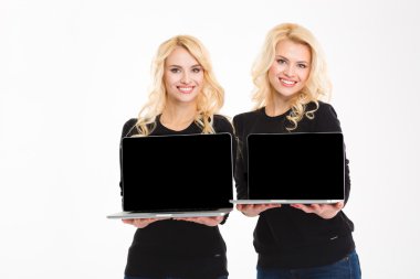 Cheerful gorgeous blonde sister twin holding blank laptop computer screen 