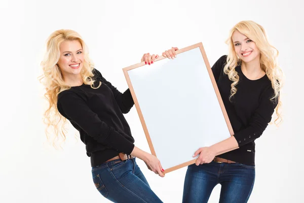 Sorrindo irmãs gêmeos segurando placa em branco — Fotografia de Stock