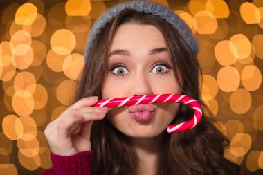 Amusing cute curly girl making funny face using candy cane 