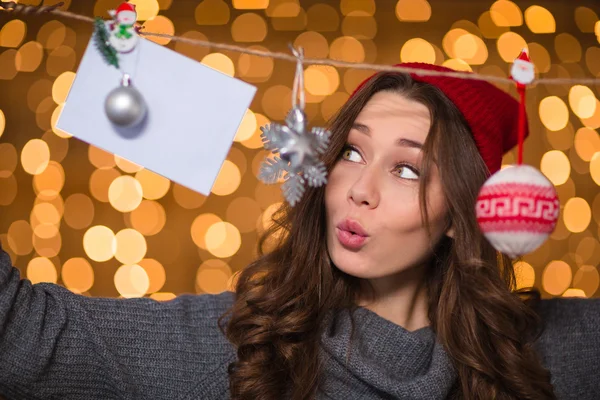 Thoughtful amusing female using handmade christmas decoration over glittering background — Stockfoto