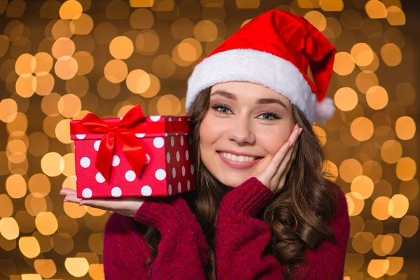 Träumend lächelnde Frau mit Geschenk auf Handfläche vor glitzerndem Hintergrund — Stockfoto