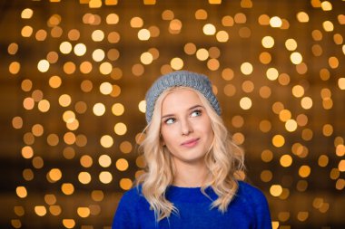Happy thoughtful woman standing over holidays lights background