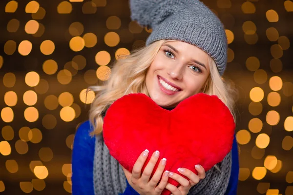 Mujer feliz sosteniendo el corazón rojo sobre las luces de las fiestas fondo —  Fotos de Stock