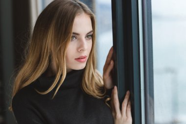 Çekici dalgın genç kadın pencereden dışarı bakıyor