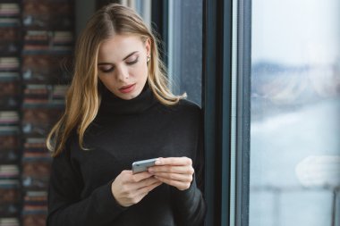 Pencerenin duran ve onun smartphone kullanarak Thougtful kadın 