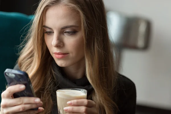 Hezká žena, pomocí mobilního telefonu a pití kávy — Stock fotografie