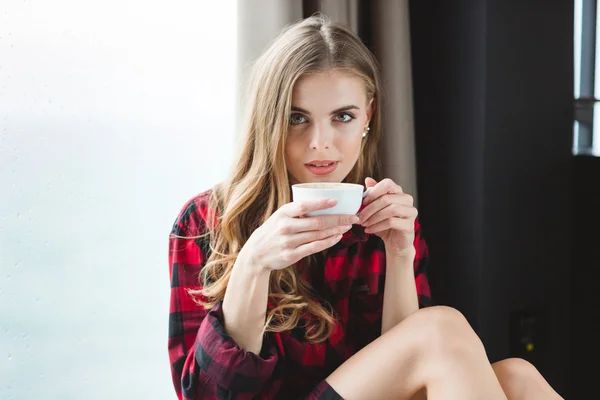 Hermosa mujer joven reflexiva en camisa a cuadros bebiendo café —  Fotos de Stock