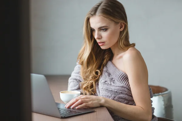 Продумана приваблива дівчина п'є каву і використовує ноутбук — стокове фото