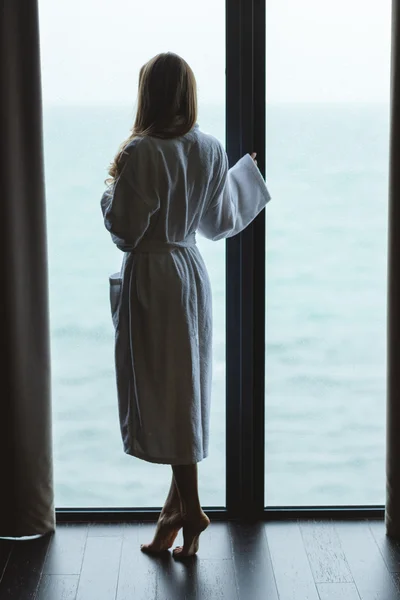 Vista posteriore di bella femmina in piedi vicino alla finestra panoramica — Foto Stock