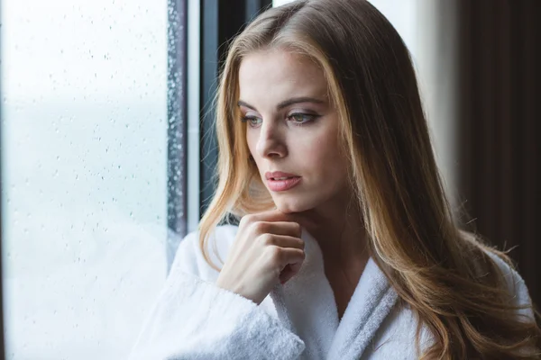 Aantrekkelijke nadenkend jonge vrouw in witte badjas op zoek — Stockfoto