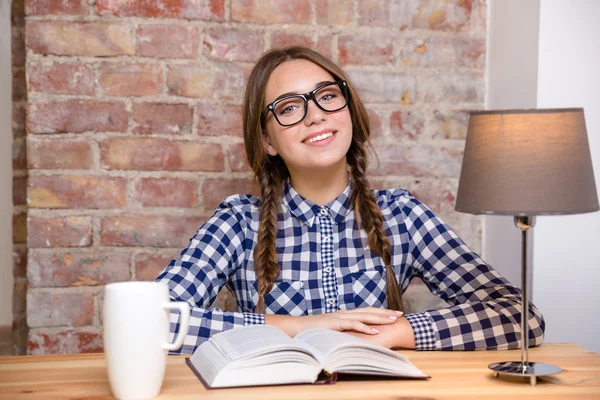 Femme heureuse dans des lunettes assis à la table avec le livre — Photo
