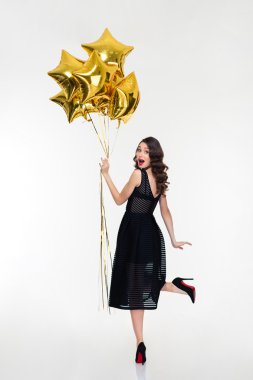 Attractive playful happy woman looking back and holding golden balloons