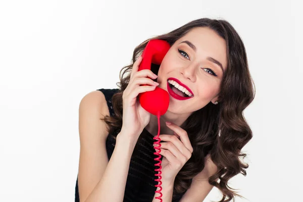 Cheerful attractive curly retro styled woman talking on red telephone — 图库照片