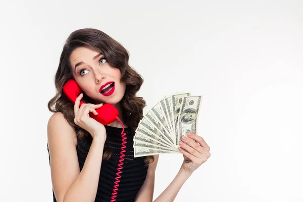 Attractive joyful curly female holding money and talking on telephone — Stockfoto