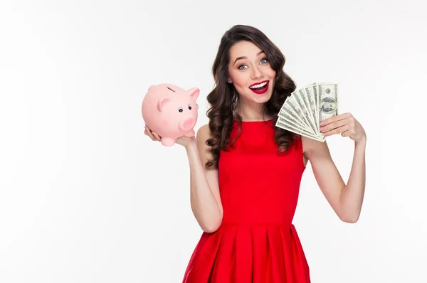 Attractive happy young curly woman holding piggy bank and money — Stockfoto