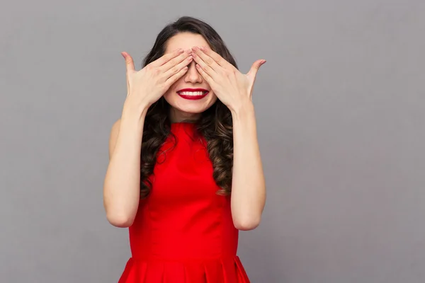 Smiling woman in red dress covering her eyes — Zdjęcie stockowe