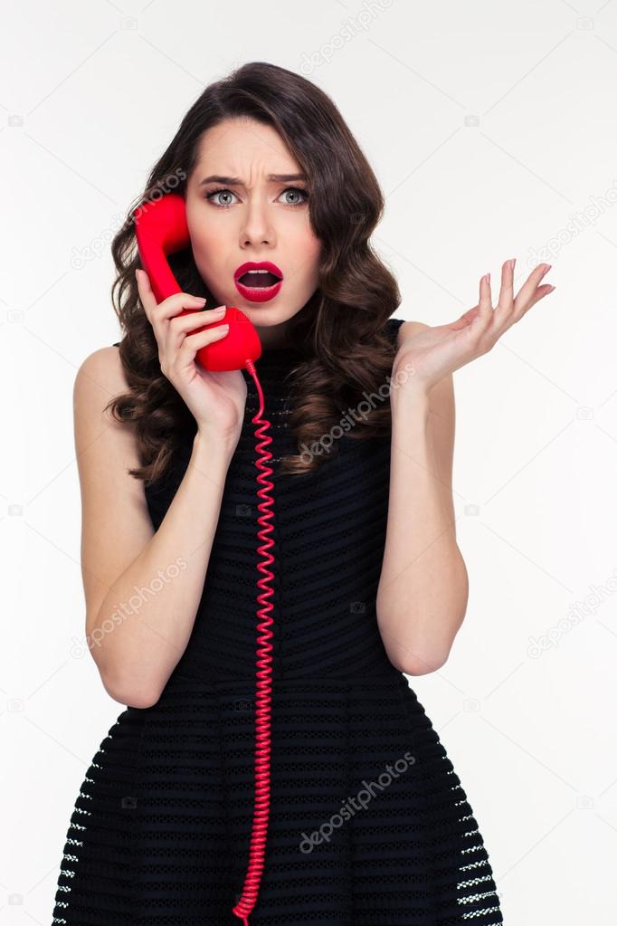 Shocked astonished beautiful retro styled woman talking on red telephone