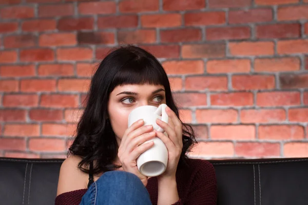 Pretty cute young woman drinking hot tea on sofa — Stockfoto