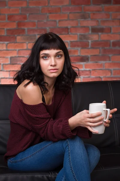 Charming thoughtful young woman sitting on couch and drinking tea — Stock Photo, Image