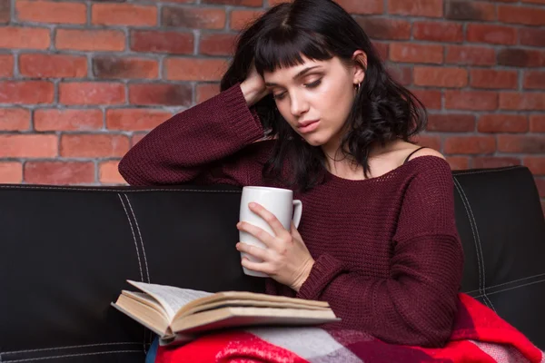 Atraente pensivo jovem mulher ler livro e beber chá — Fotografia de Stock