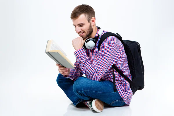 Cheerful handsome bearded man with backpack and headphones reading book — Stock Photo, Image