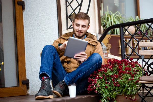 Uomo barbuto sorridente seduto sul portico vicino all'ingresso utilizzando tablet — Foto Stock