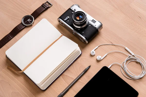 Notatnik, tabletki, słuchawki, kamera zegarek i pióra na drewnianym stole — Zdjęcie stockowe