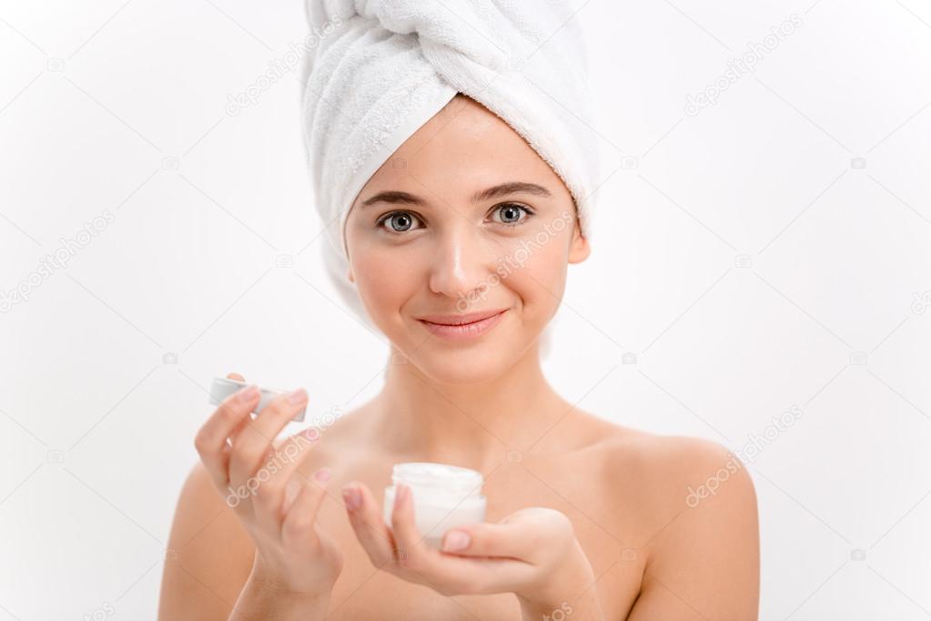 Beautiful female with towel on her head using face cream