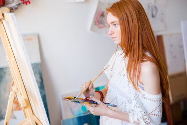Concentrated pensive woman painter with long hair painting on canvas 