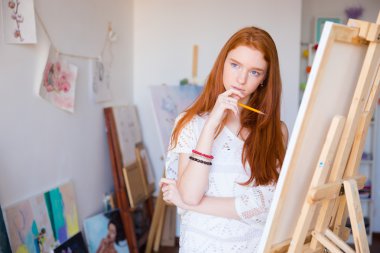 Attractive pensive female artist thinking and drawing on canvas 