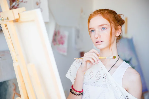 Thoughtful woman painter standing in front of easel with paintbrush — Stock Photo, Image