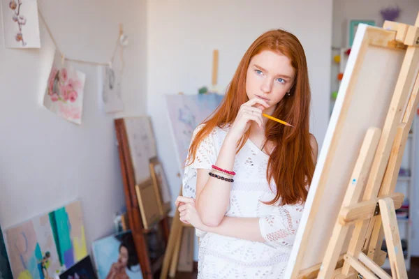Attractive pensive female artist thinking and drawing on canvas — Stockfoto