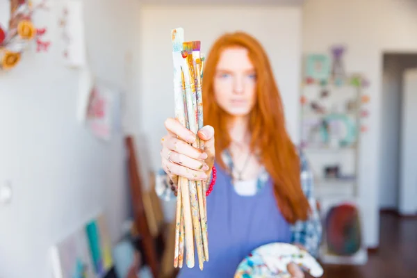 Pinceles sostenidos por la joven pelirroja pintora en taller de artista — Foto de Stock