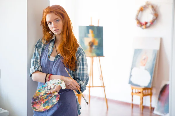 Удумлива молода жінка живописець тримає художню палітру і пензлик — стокове фото