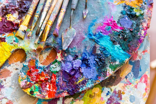 Närbild av konst palett med färgglada blandade färger och målade borstade — Stockfoto