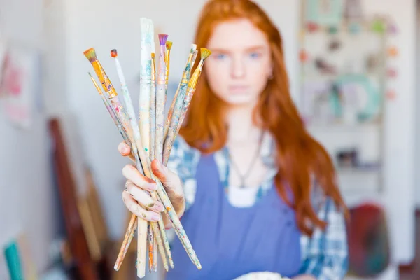 Young woman painter showing dirty paintbrushes in artist workshop — Stockfoto