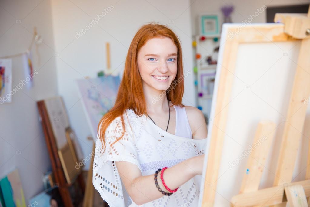 Cheerful attractive woman artist painting on canvas in art workshop