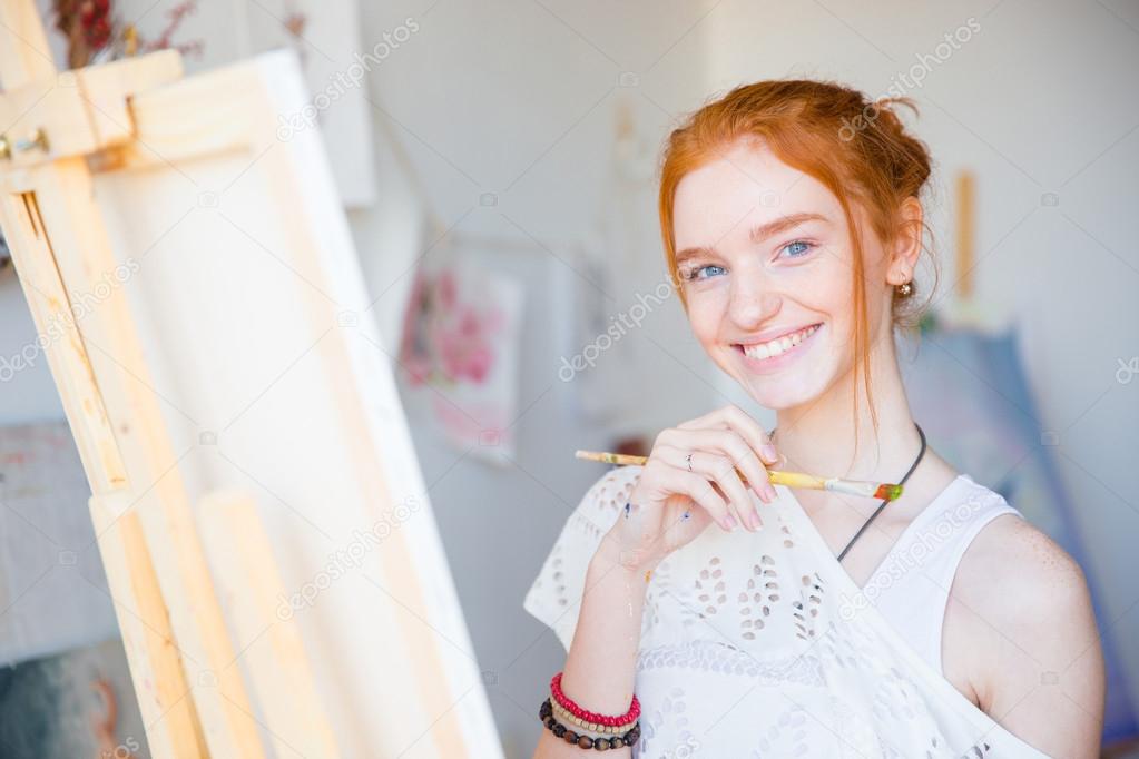 Cheerful charming young female artist painting  with paintbrush on canvas 