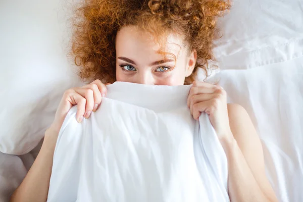 Shy cute lovely young woman hiding her face behind sheet — Stock fotografie