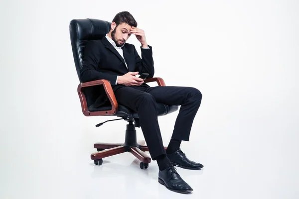 Empresario concentrado sorprendido sentado en la silla de la oficina y usando el teléfono inteligente —  Fotos de Stock