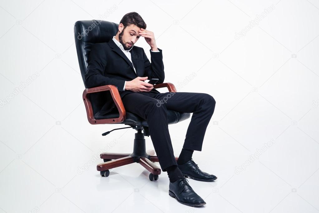Amazed concentrated businessman sitting in office chair and using smartphone